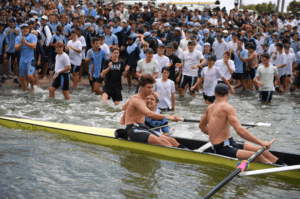 Rowers celebrating a win while sitting in their rowing boat on the water as spectators and fans cheer them on